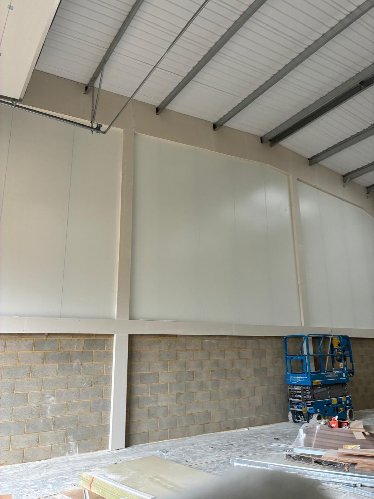 Lining panels fixed to the warehouse wall above the blockwork course