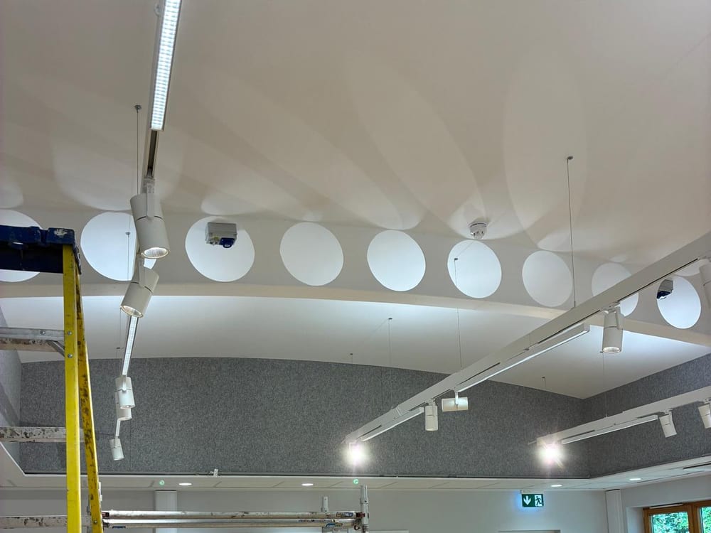 Hall with grey acoustic ceiling rafts, circular acoustic discs and track lighting, with a mobile tower still in place