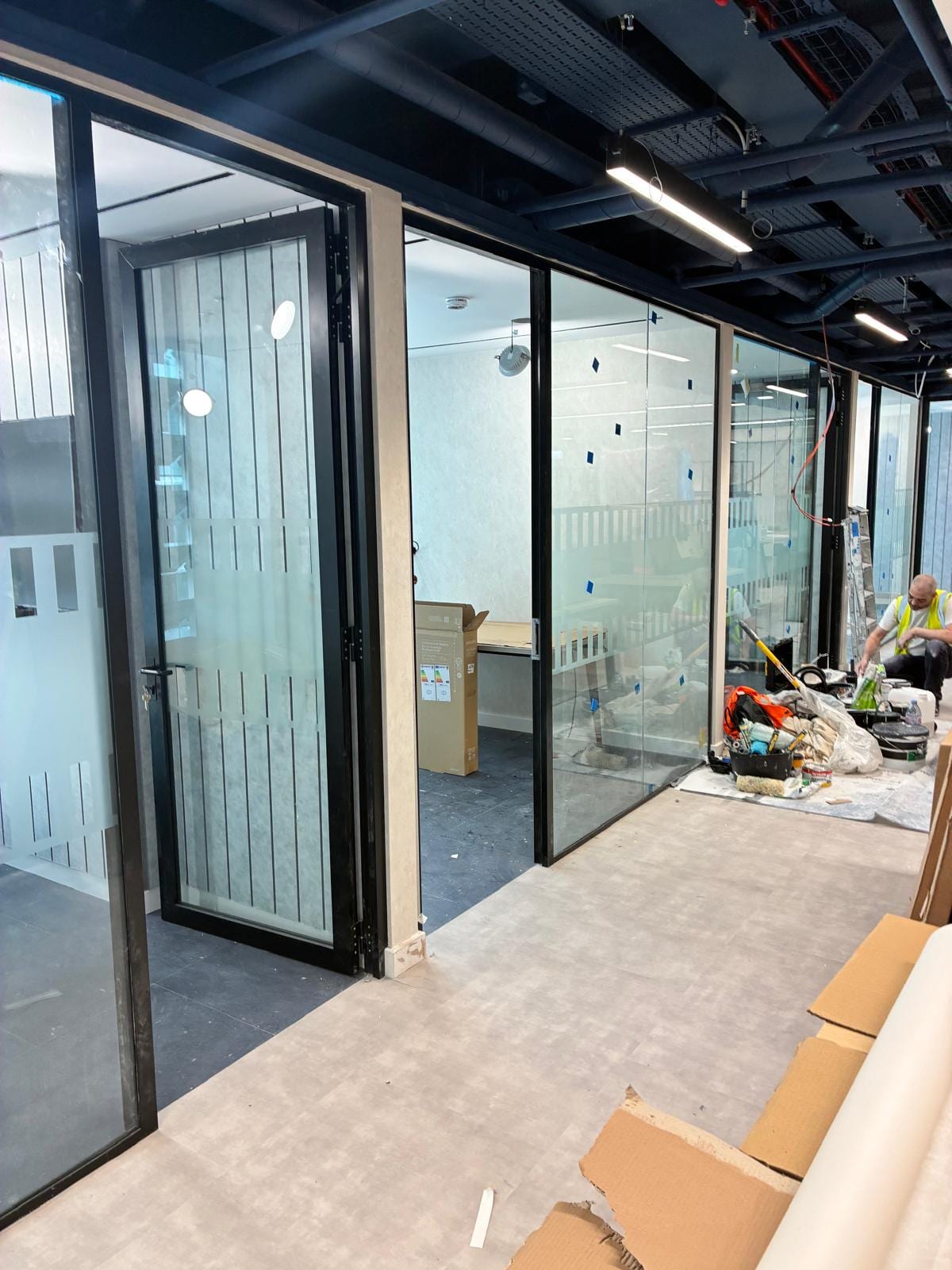 Black framed glass partitions under a dark painted soffit with the services on show